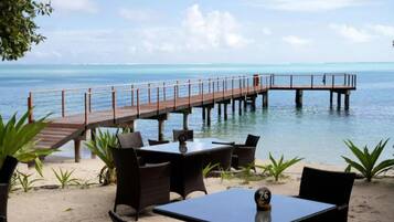 Een restaurant aan het strand met terras, een houten vlonder en uitzicht op de oceaan.