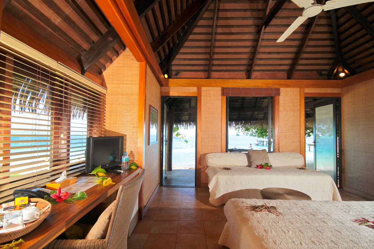 A room with a wooden desk, a television, and a bed with a white bedspread.