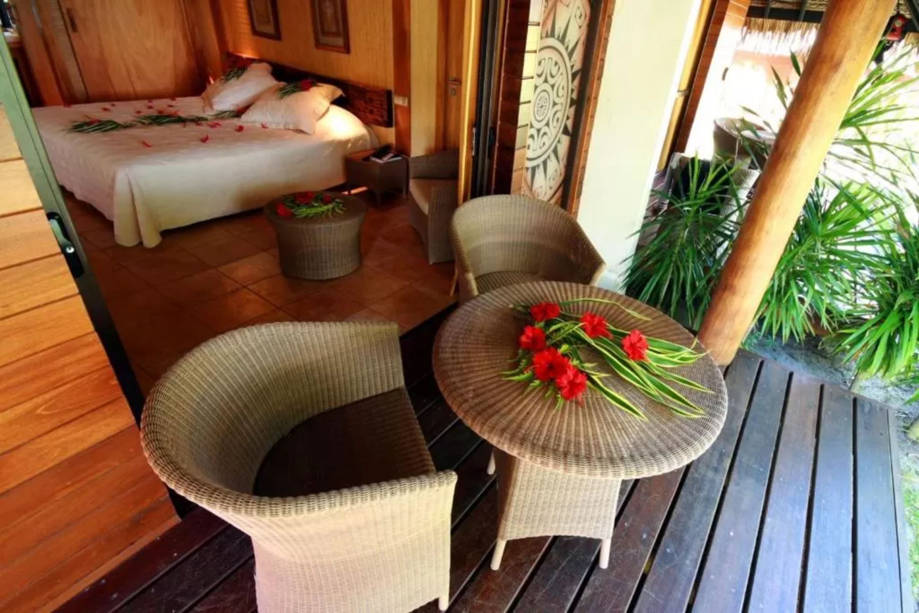 A cozy room with a bed, wicker chairs, a small table with flowers, and a wooden floor.