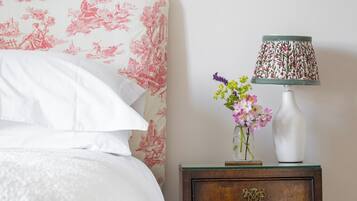 A bedroom with a bed, a nightstand with a lamp, and a vase with flowers.