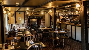 A cozy restaurant with brick walls, wooden tables, and a bar area with bottles and glasses. - The Brace of Pheasants (Dorchester)