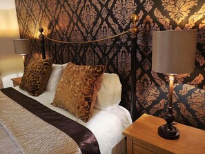A bed with patterned pillows, a bedside lamp, and a wall with a damask pattern. - Glangwili Mansion (Carmarthen)