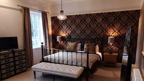 A bedroom with a bed, bedside tables, a television, and a radiator. - Glangwili Mansion (Carmarthen)