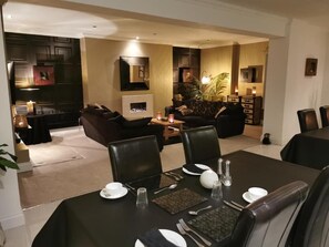A dining area with a table set for four, a sofa, and a fireplace in the background. - Glangwili Mansion (Carmarthen)