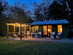 A cozy outdoor patio with wicker furniture and string lights, adjacent to a wooden cabin with glass doors. - Glangwili Mansion (Carmarthen)