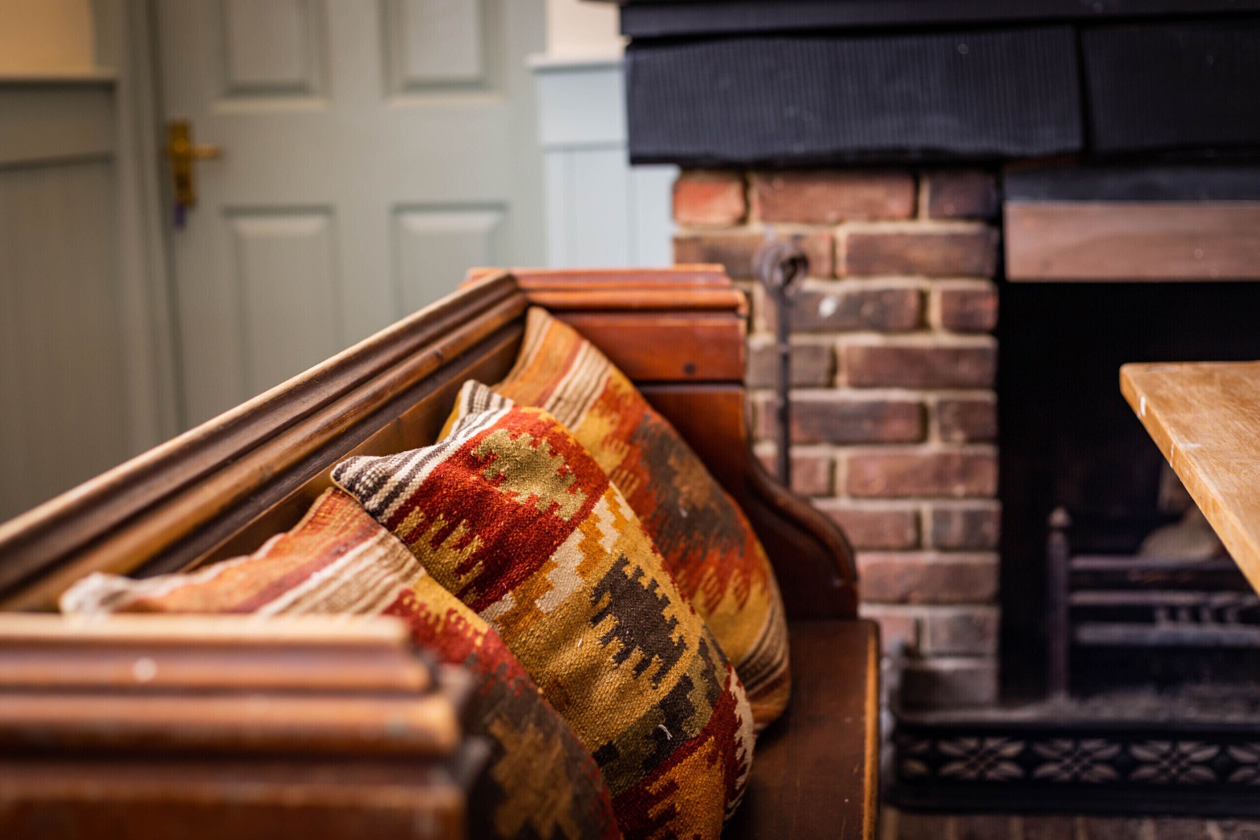 A wooden bench with a colorful woven cushion in front of a brick fireplace.