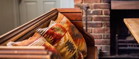 A wooden bench with a colorful woven cushion in front of a brick fireplace.