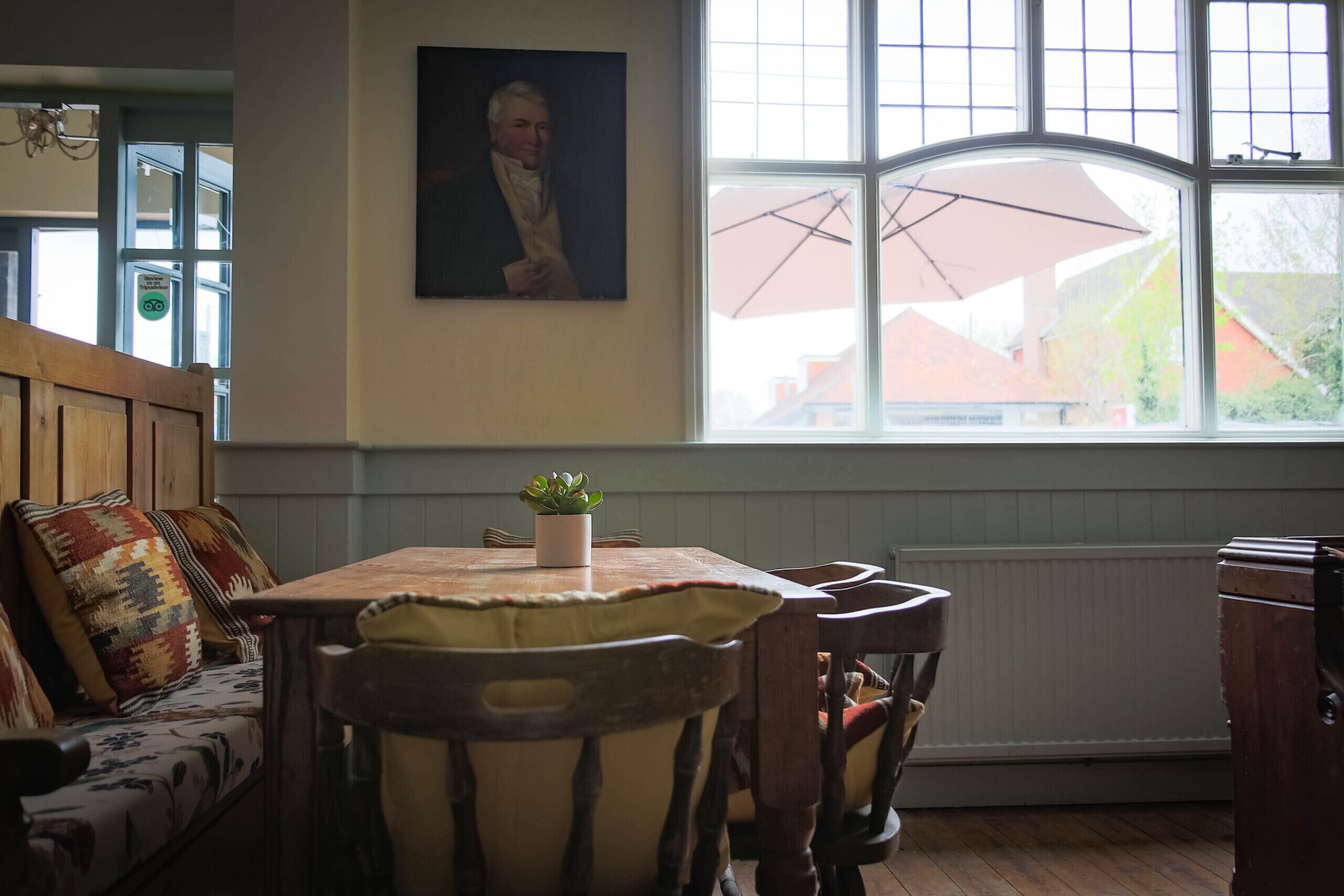 A cozy dining area with a wooden table and chairs, a potted plant, and a painting on the wall.