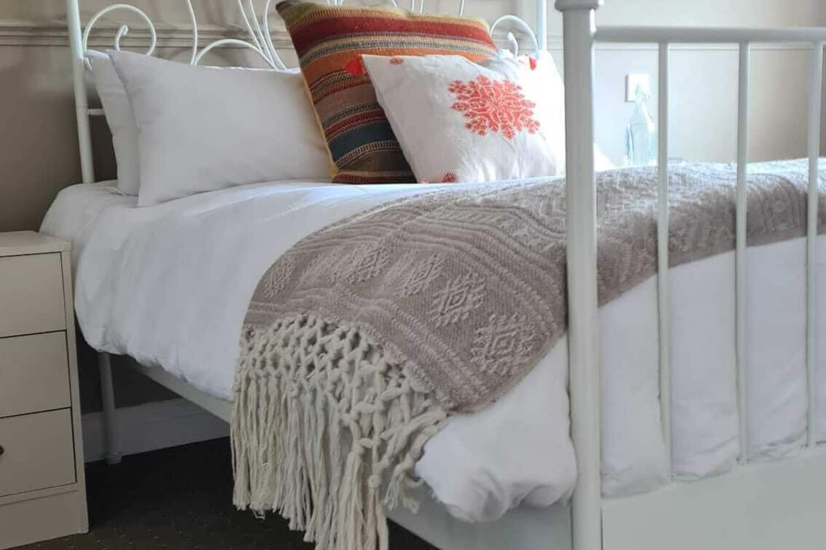 A white metal bed with a headboard, a bedside table, and a wall-mounted lamp.