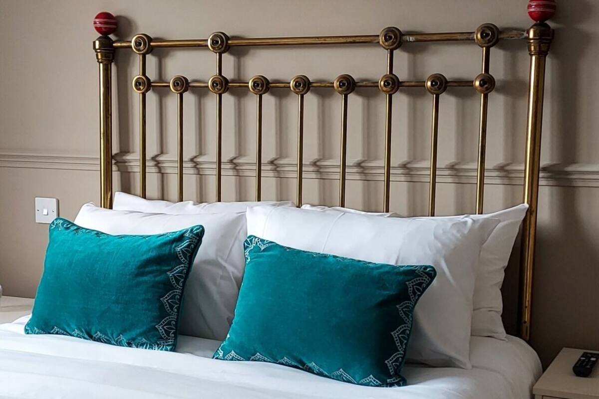 A neatly made bed with a gold headboard, white bedding, and teal pillows.