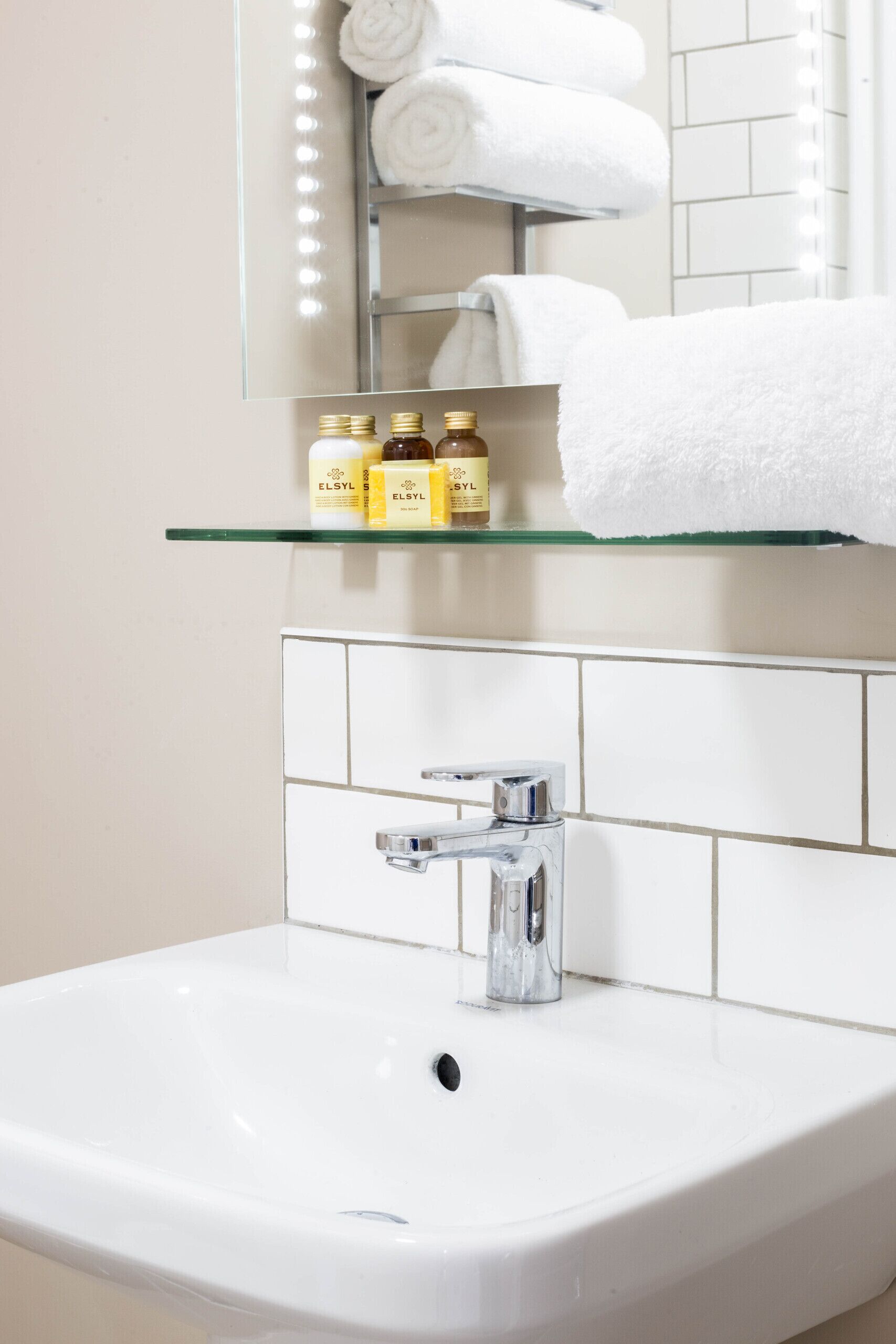 A bathroom with a white sink, a mirror, and a shelf with toiletries.