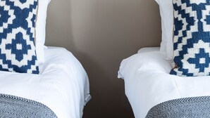 Habitación de hotel con dos camas, cada una con almohada estampada, una lámpara de pared y una pared lisa.