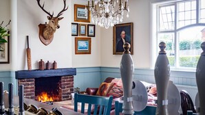Una habitación con chimenea, un ciervo montado como adorno, cuadros enmarcados y una ventana con vistas.