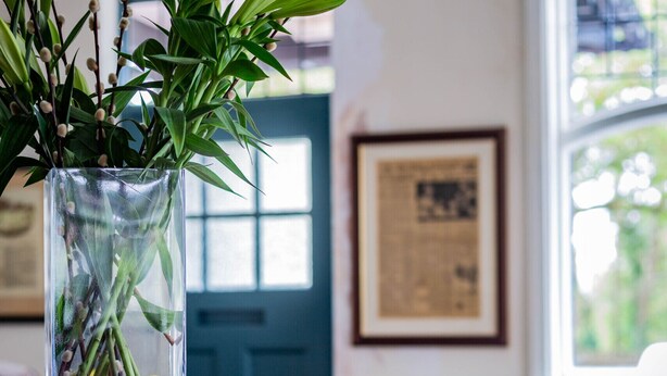 Un jarrón de cristal transparente con hojas verdes y flores amarillas sobre una encimera de madera.