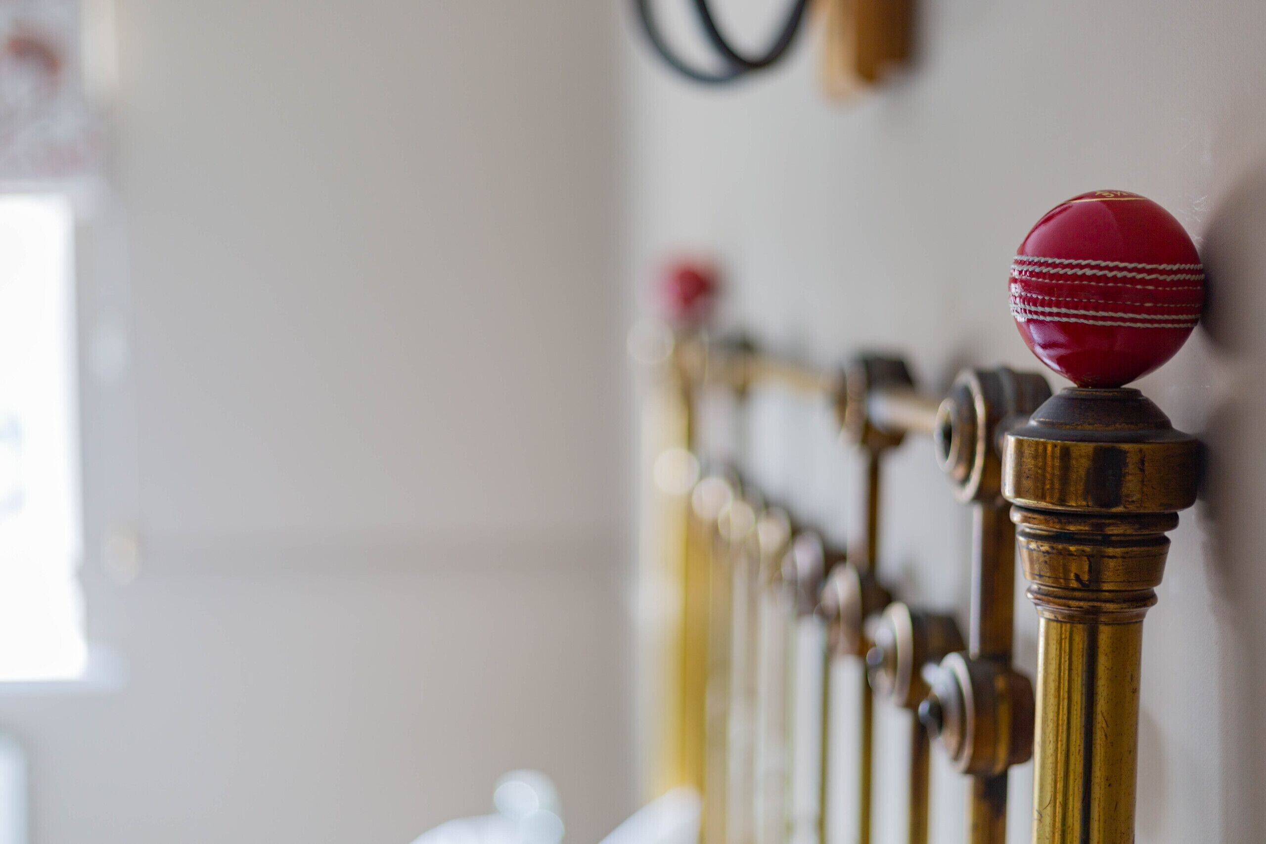 A close-up of a red cricket ball on a brass cricket bat.