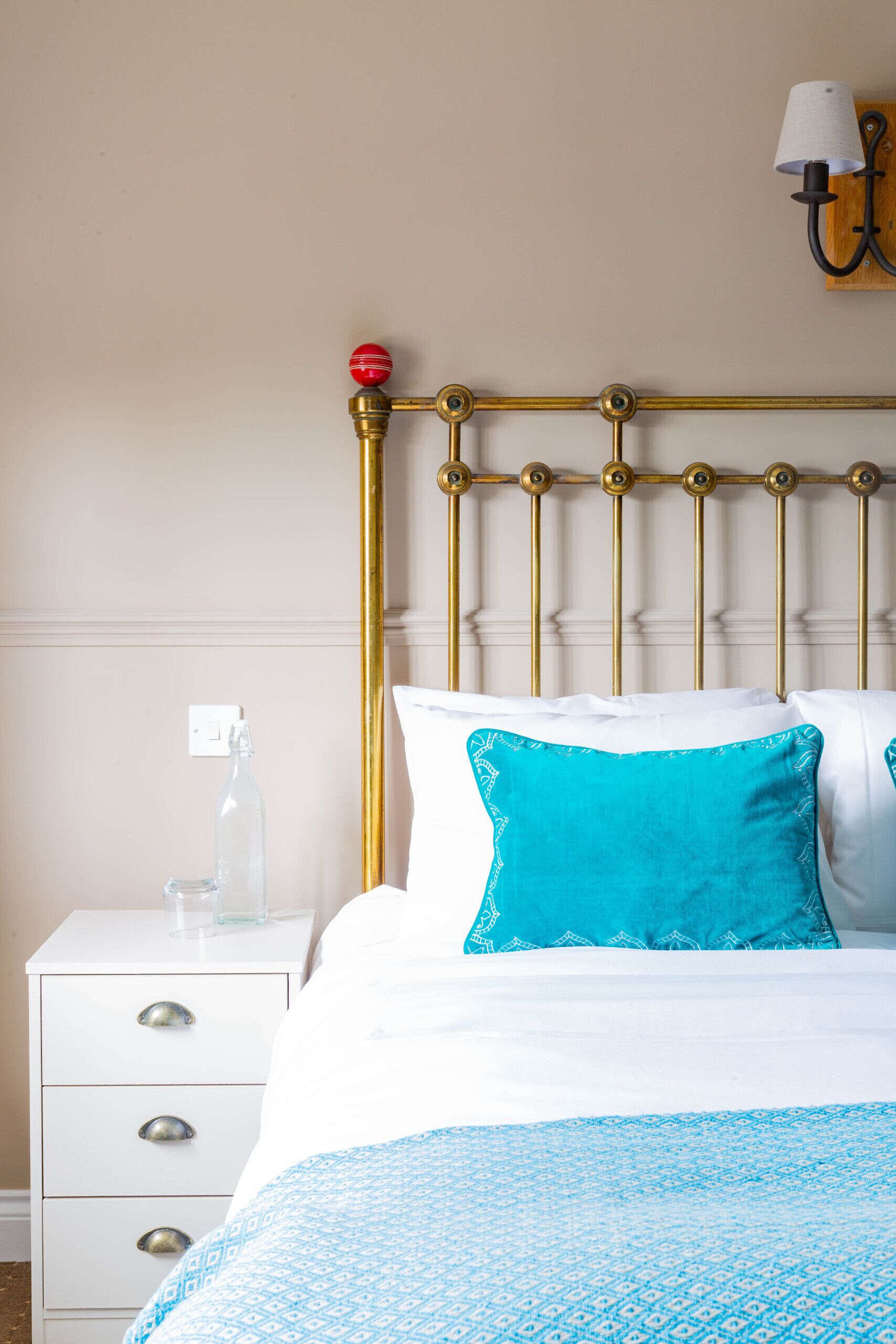 Un lit bien fait, recouvert d’une courtepointe bleue à motifs, avec un oreiller blanc et un oreiller turquoise.