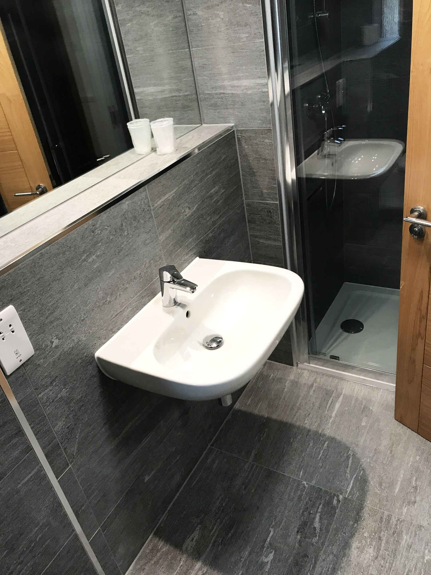 A modern bathroom with a white sink, dark tiled walls, and a glass shower enclosure.