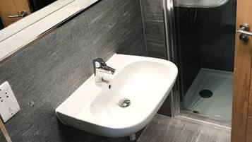 A modern bathroom with a white sink, dark tiled walls, and a glass shower enclosure.