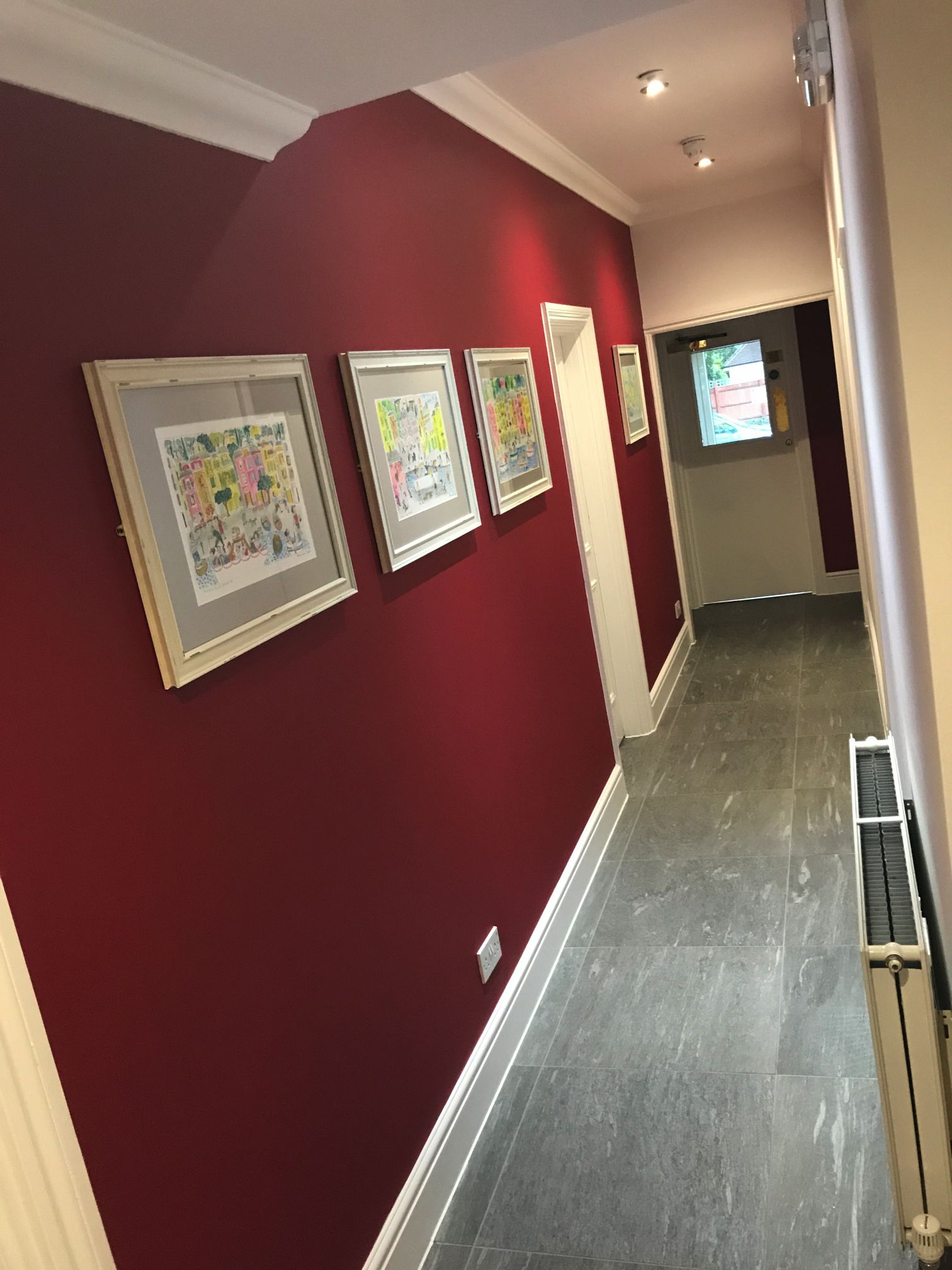 A hallway with red walls and a tiled floor, featuring framed artworks on the wall.