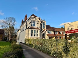 A traditional Tudor-style building with a prominent entrance, a sign advertising free parking and WiFi, and a well-maintained hedge-lined driveway.