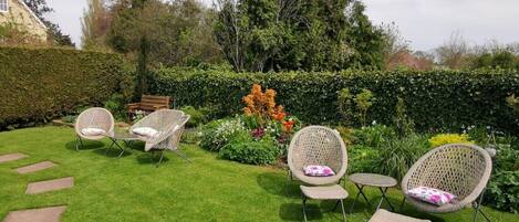 Un jardín bien cuidado con césped, varias sillas de mimbre y un banco.