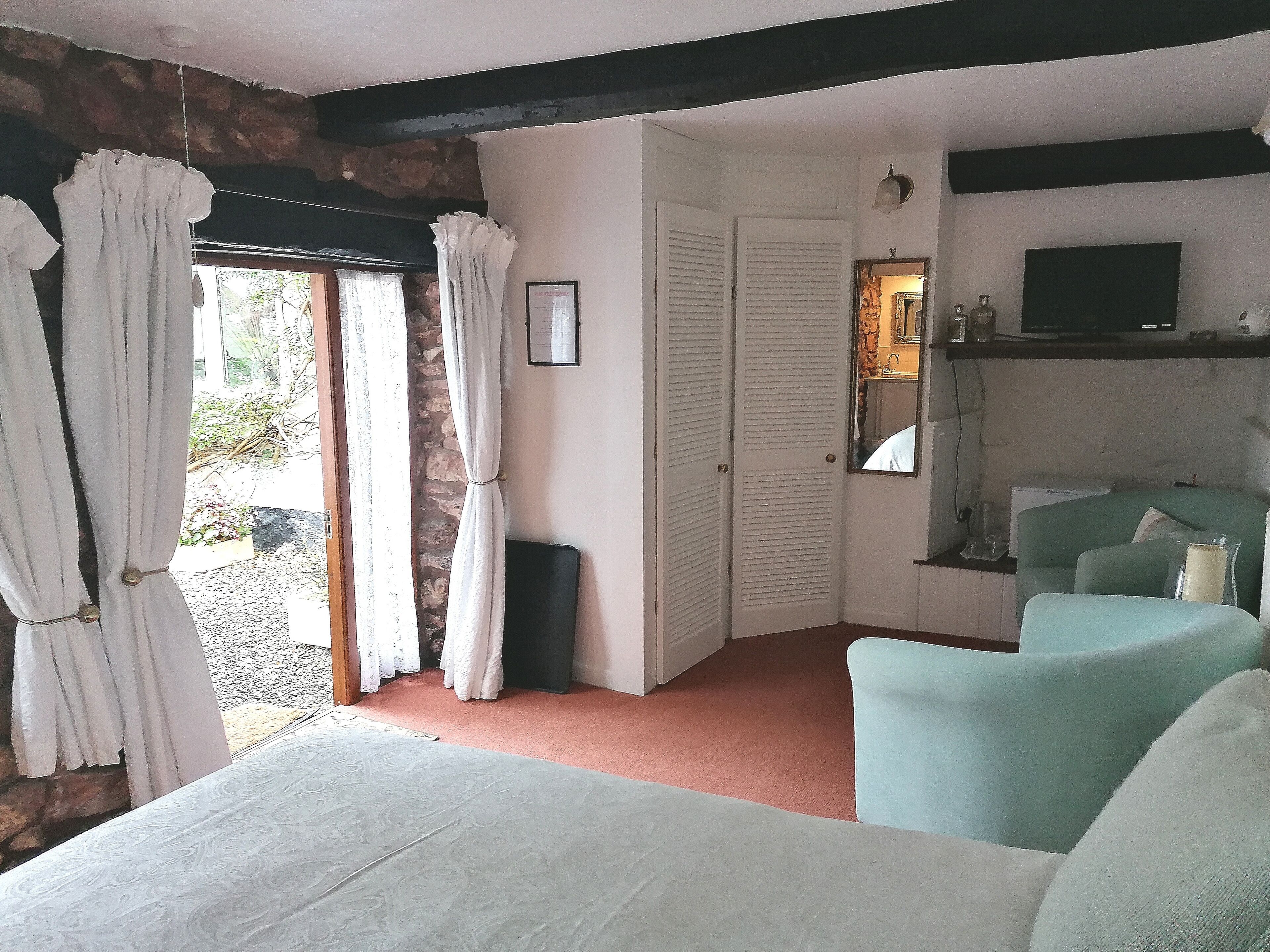 A room with a bed, a seating area with chairs, a television, and a door leading to a bathroom.