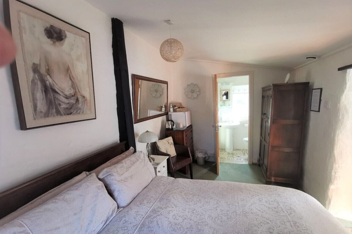A bedroom with a large bed, a dresser, a mirror, and a door leading to a bathroom.