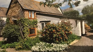 A traditional stone house with a sloped roof, a wooden ladder, and a small window. - Steps Farmhouse (Minehead)