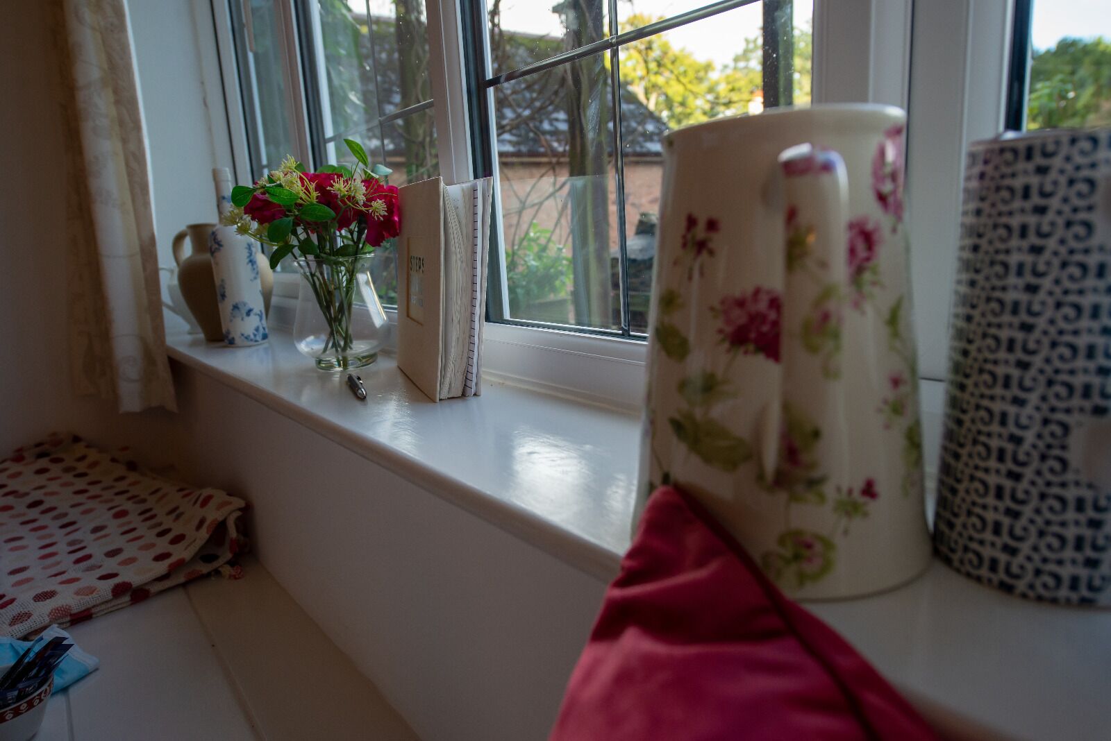 A window sill with a vase of flowers, a patterned mug, and a small decorative item.