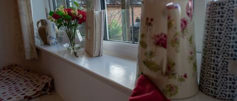 A window sill with a vase of flowers, a patterned mug, and a small decorative item.