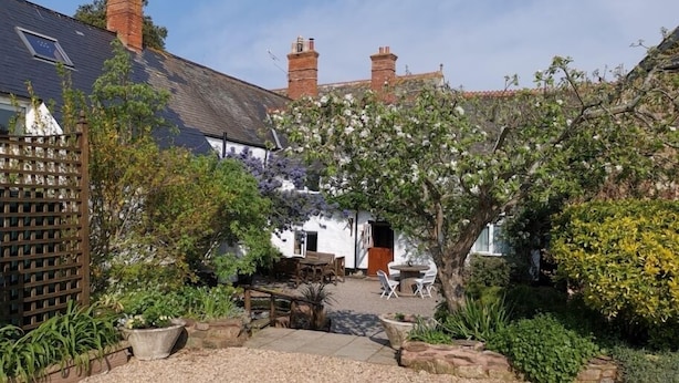 A garden with a gravel path leading to a white building with a dark roof. - Steps Farmhouse (Minehead)