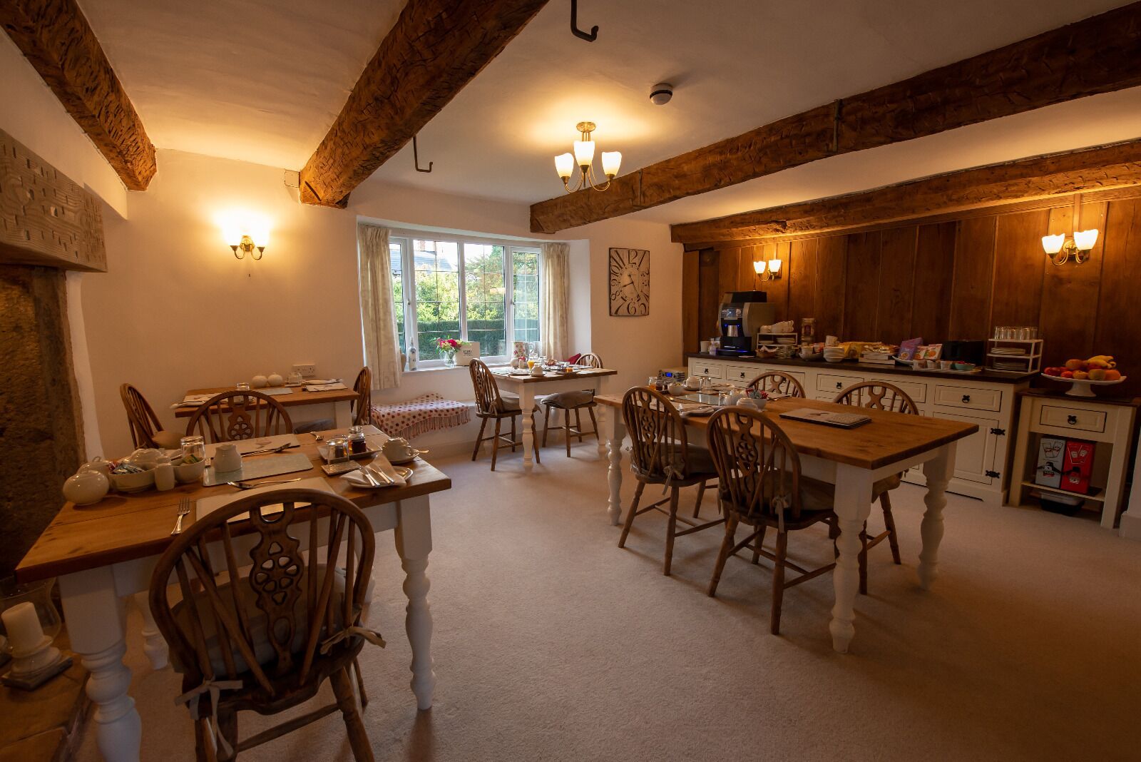 A cozy dining area with wooden tables and chairs, a kitchen with wooden cabinets, and a large window providing natural light.
