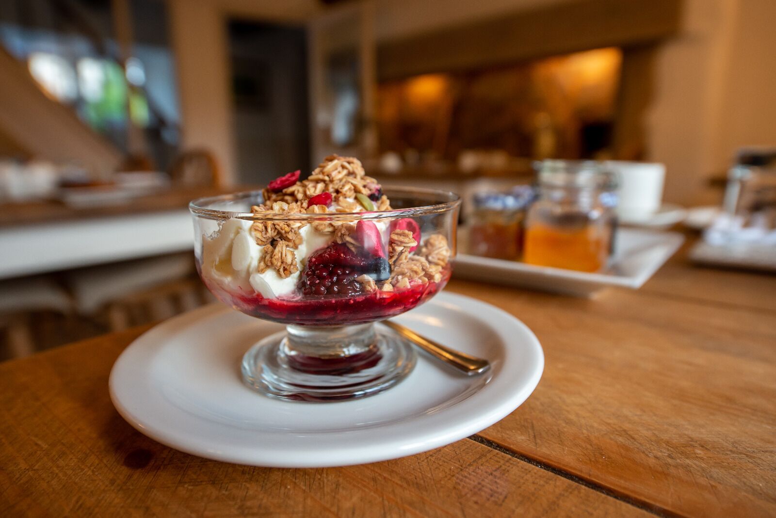A dessert in a glass bowl on a white plate, with a spoon beside it.