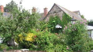 A traditional stone house with a thatched roof, surrounded by lush greenery and flowering plants. - Steps Farmhouse (Minehead)