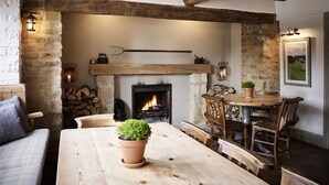 A rustic interior with exposed wooden beams, a fireplace, a dining table with chairs, and a sofa. - The Masons Arms (Cirencester)
