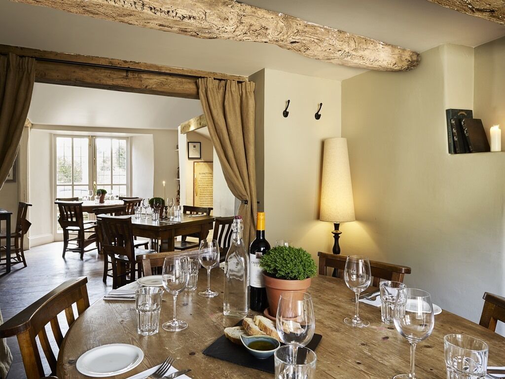 Un comedor con una mesa de madera dispuesta para una comida, una planta en maceta y botellas de vino.