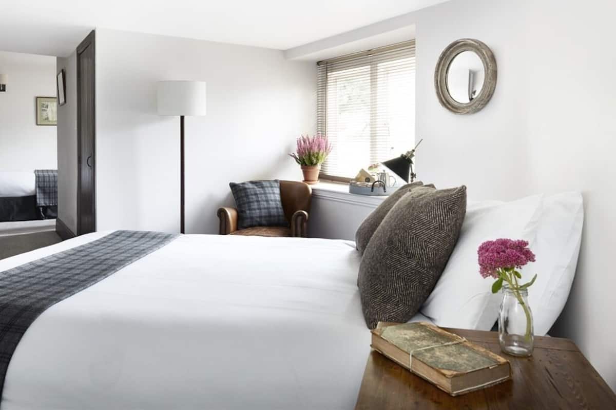 Una habitación de hotel con una cama grande, un escritorio con lámpara, una silla, una ventana con persianas y un espejo en la pared.