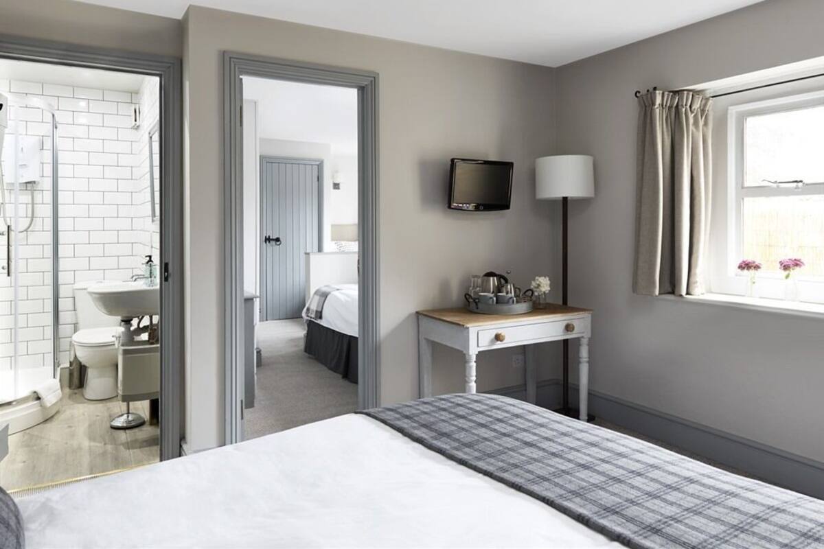 Habitación de hotel con cama, mesita de noche con lámpara, televisor y ventana con cortinas.