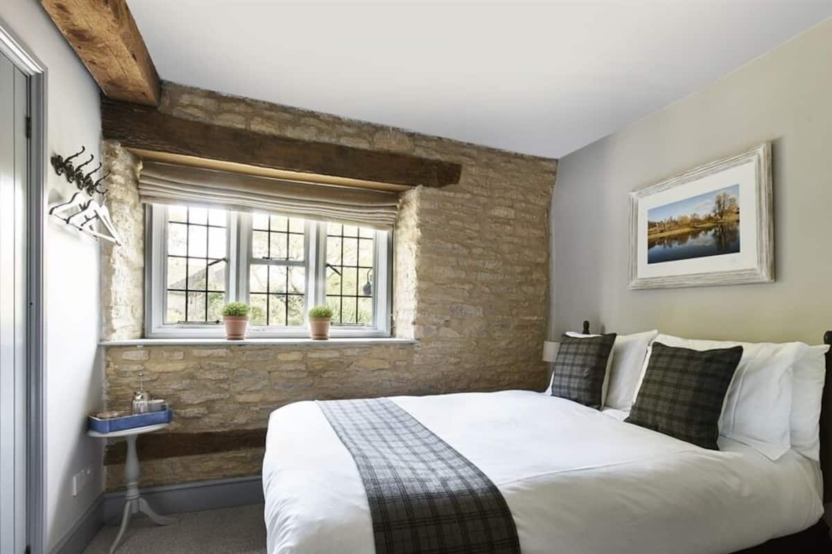 Un dormitorio con una cama grande, una pared de piedra, una ventana con plantas y un cuadro en la pared.