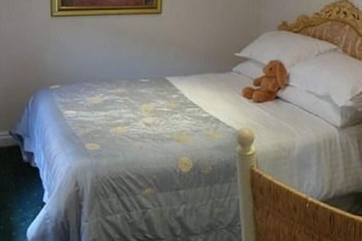 A bed with a wooden headboard, a teddy bear on the pillows, and a framed picture on the wall.