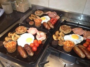 A breakfast spread with various items like eggs, sausages, and tomatoes on a stovetop.