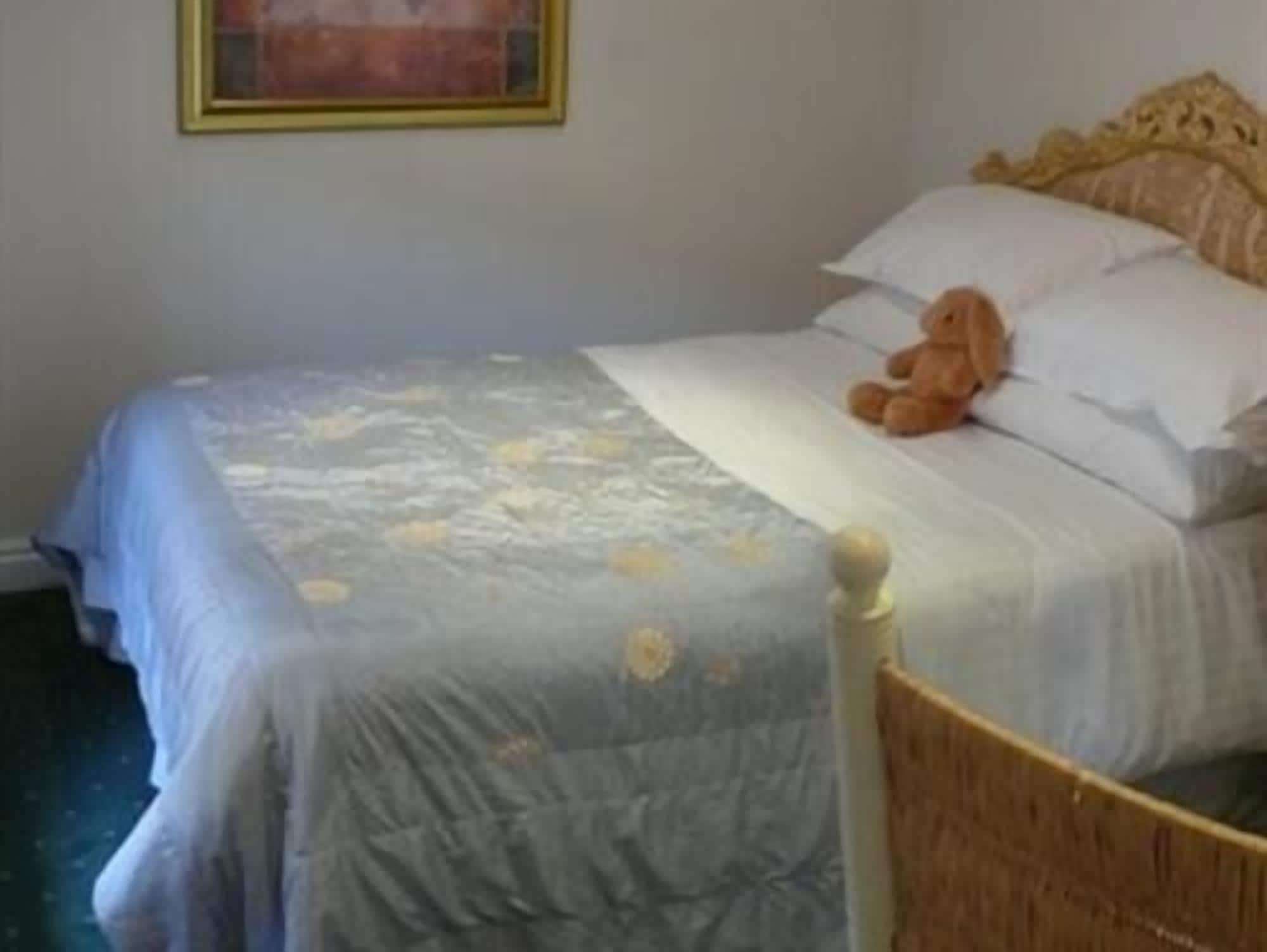 Una cama con colcha azul, un osito de peluche y un cabecero de madera.