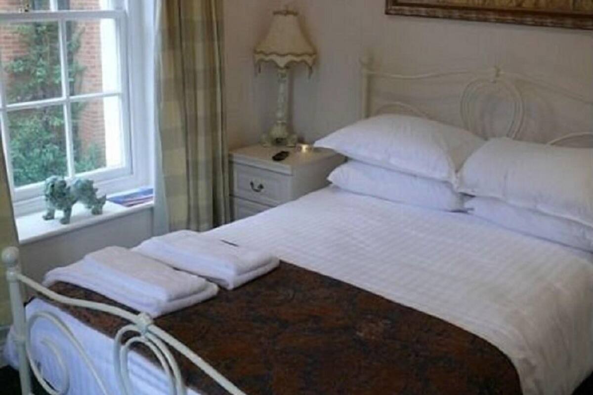 A neatly made bed with white linens, a bedside lamp, and a window with a view of greenery.