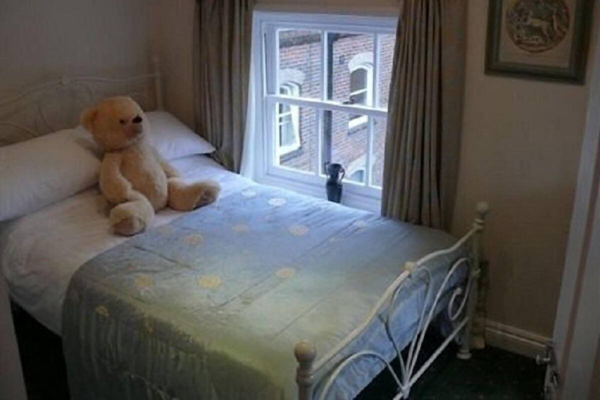 A bedroom with a bed, a window, and a teddy bear.