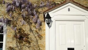 A white door with the number 8, a black mailbox, and a stone wall with purple flowers. - The Heritage Bed & Breakfast (Weymouth)