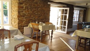 A dining area with wooden tables and chairs, stone walls, and large windows. - The Heritage Bed & Breakfast (Weymouth)