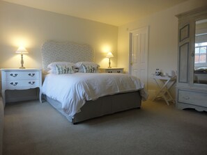 A neatly arranged bedroom with a bed, two bedside tables with lamps, a small side table, and a wardrobe.