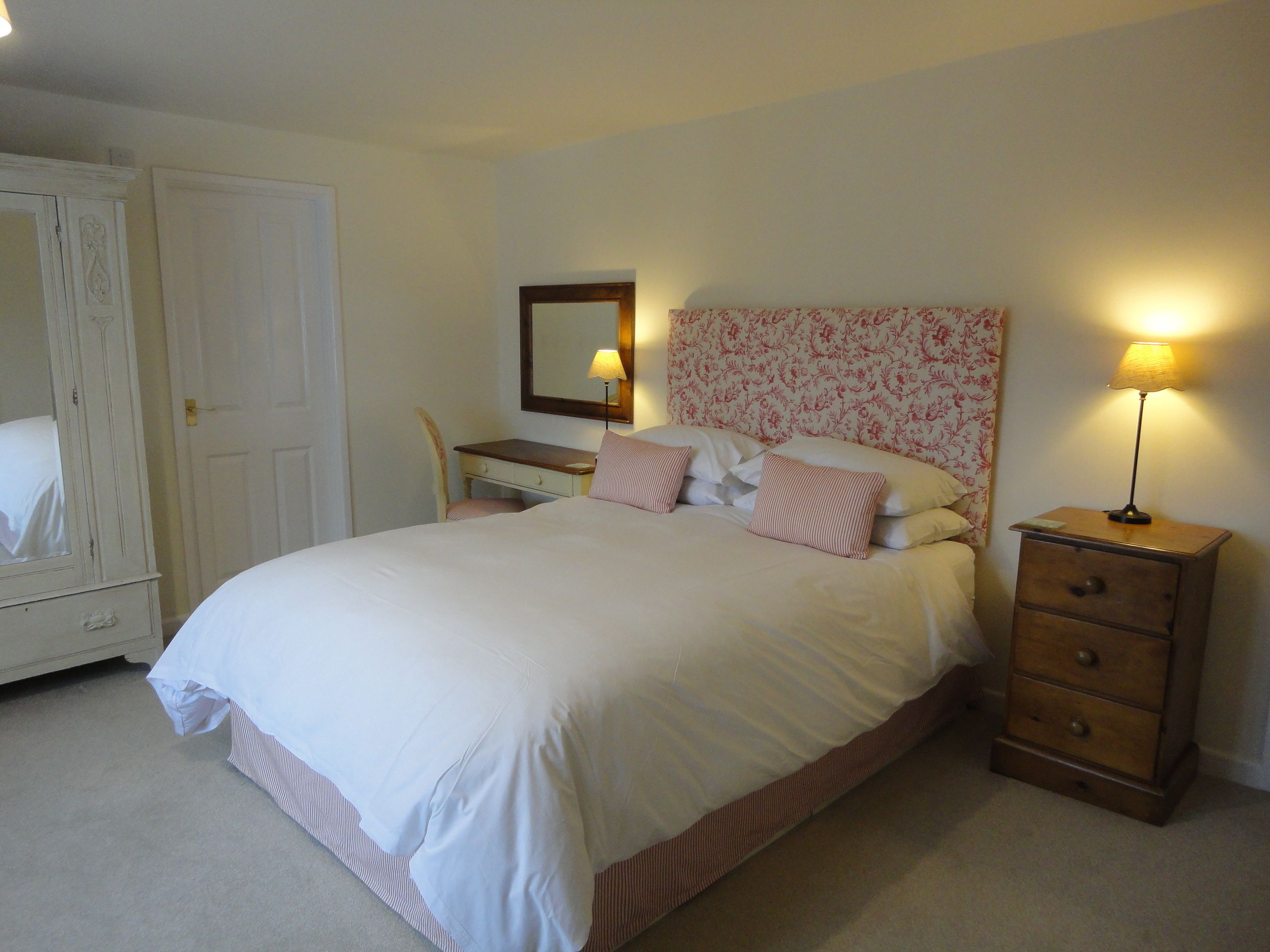 A neatly made bed with a headboard, a bedside table with a lamp, a chair, and a wardrobe.