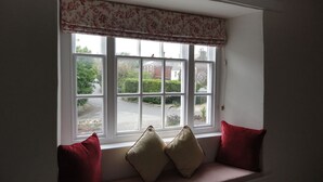 A window with a view of a road and greenery, a bench with cushions, and a floral valance. - The Heritage Bed & Breakfast (Weymouth)