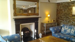A living room with a fireplace, blue patterned sofa, wooden coffee table, and a stone wall. - The Heritage Bed & Breakfast (Weymouth)